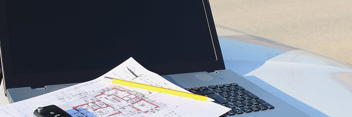 Symbolbild: Ein aufgeklappter Laptop mit einem ausgedruckten Bauplan auf der Tastatur. 