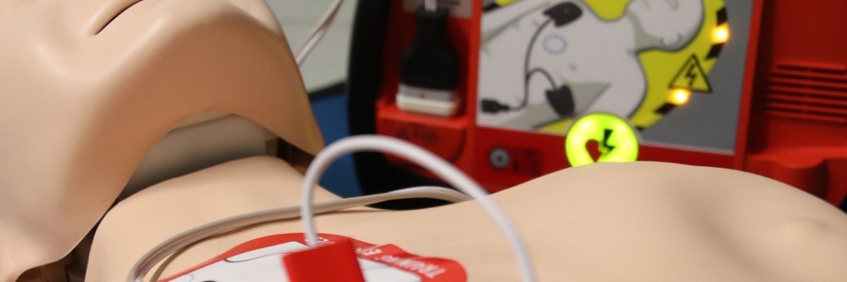 Symbolbild: Eine Übungspuppe für Wiederbelebung liegt auf dem Boden und ist an einen tragbaren Defibrillator angeschlossen.
