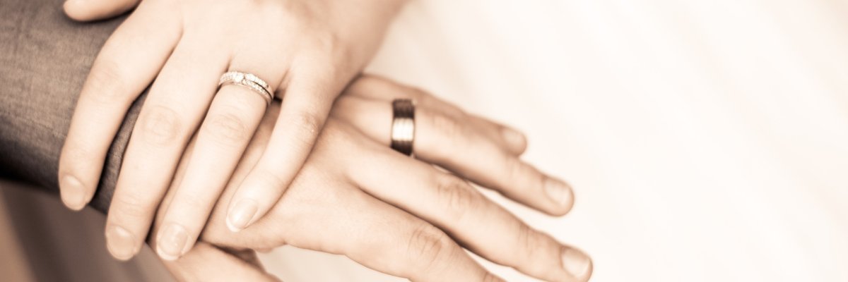 Symbolbild: Foto von zwei liebevoll übereinandergelegten Händen mit Ringen